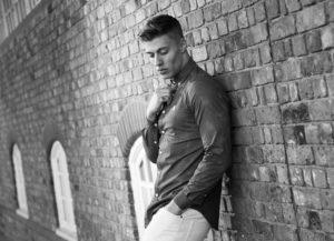 male model leaning on brick wall
