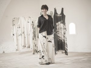 Woman stands in front of hung clothes